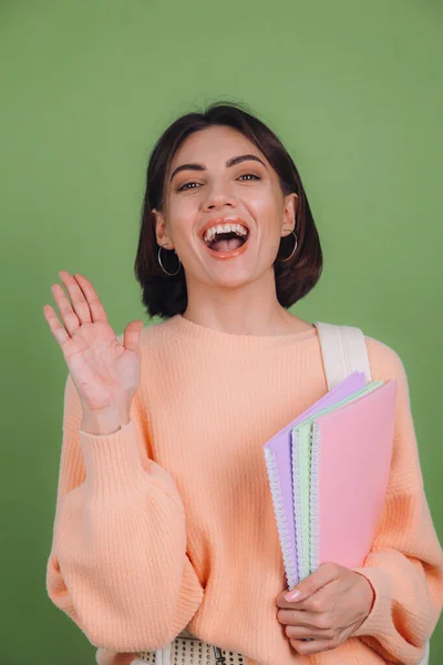 Young woman in casual peach sweater and backpack isolated on green olive color background surprised excited emotions mouth open, education concept