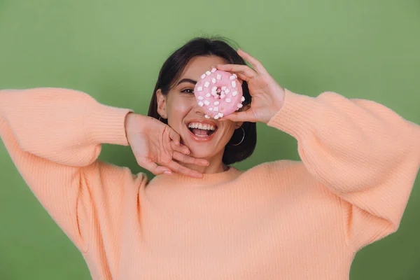 Young stylish woman in casual peach sweater  isolated on green olive background with pink donut happy copy space