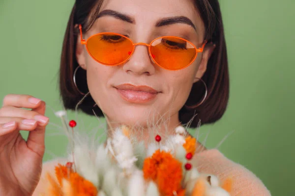 Young woman in casual peach sweater  isolated on green olive background  hold  orange white flower box composition of cotton flowers, gypsophila, wheat and lagurus for a gift happy surprised