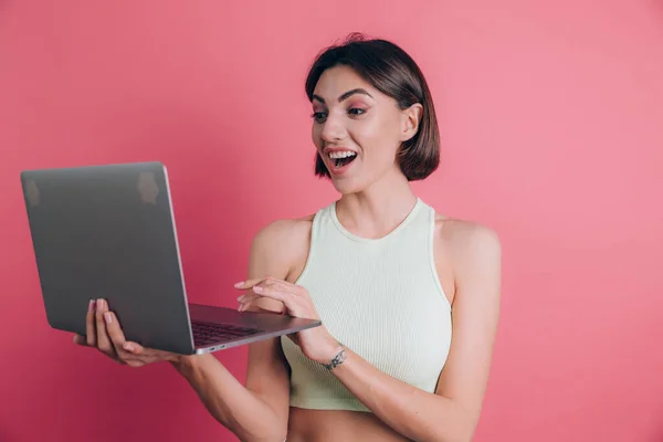 Women on pink background  keeping mouth open hold laptop computer