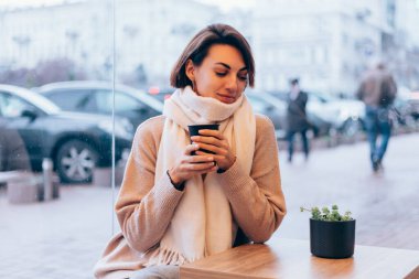 Sıcak bir kafede bir kız kendini bir fincan sıcak kahveyle ısıtıyor.