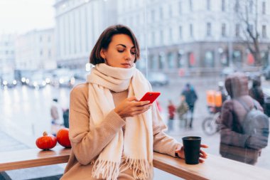 Sıcak bir kafede bir kız kendini bir fincan sıcak kahveyle ısıtıyor.