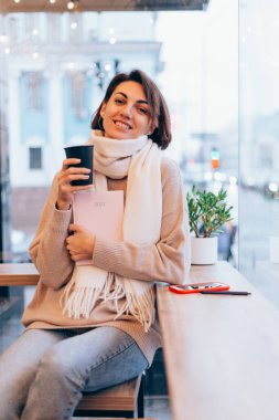 Sıcak bir kafede bir kız kendini bir fincan sıcak kahveyle ısıtıyor.