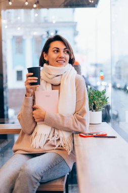 Sıcak bir kafede bir kız kendini bir fincan sıcak kahveyle ısıtıyor.