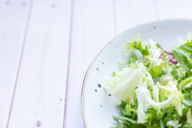 Ahşap zemin üzerinde taze salata ile beyaz seramik tabak