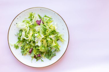 Açık pembe zemin üzerinde taze salata ile beyaz seramik tabak