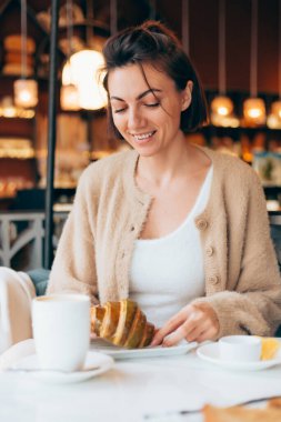 Bir kafede kahve ve kruvasanla gezen bir kız.