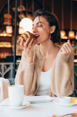 Bir kafede kahve ve kruvasanla gezen bir kız.