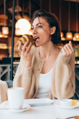 Bir kafede kahve ve kruvasanla gezen bir kız.