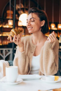 Bir kafede kahve ve kruvasanla gezen bir kız.