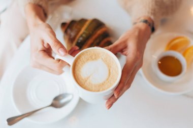 Bir kafede kahve ve kruvasanla gezen bir kız.