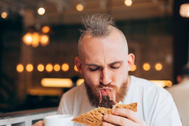 Bir kafede Avrupalı görünümlü vahşi bir adamın lezzetli bir sandviçi var.