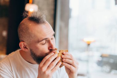 Bir kafede Avrupalı görünümlü vahşi bir adamın lezzetli bir sandviçi var.