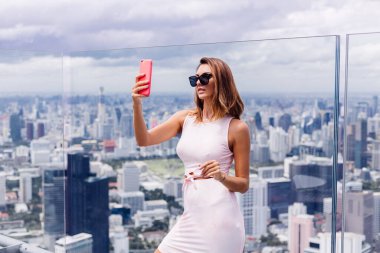 Bangkok 'un en üst katında, beyaz elbiseli ve güneş gözlüklü beyaz kadın gezgin.