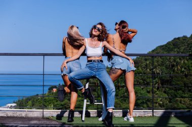 Üç bronz tenli mutlu kadın arkadaş birlikte gülümser ve güler.