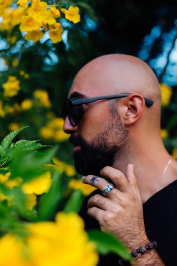 Güneş gözlüklü sakallı adamın parmağında palmiye ağacı dövmesi var.