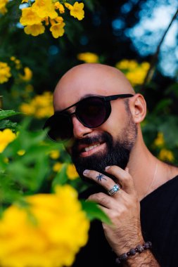 Güneş gözlüklü sakallı adamın parmağında palmiye ağacı dövmesi var.