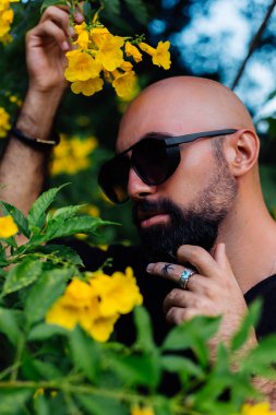 Güneş gözlüklü sakallı adamın parmağında palmiye ağacı dövmesi var.