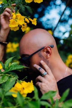 Güneş gözlüklü sakallı adamın parmağında palmiye ağacı dövmesi var.