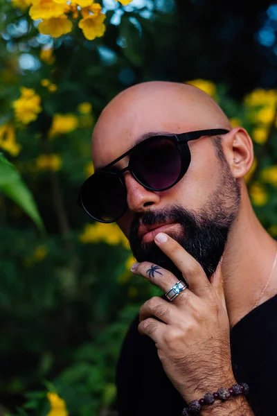 Güneş gözlüklü sakallı adamın parmağında palmiye ağacı dövmesi var.