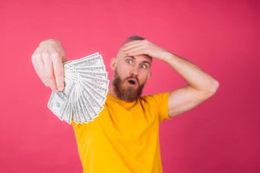 Pembe arka plandaki Avrupalı adam 100 dolarlık fanı ile şok oldu. Alnına dokunuyor ve ağzı açık kalıyor.