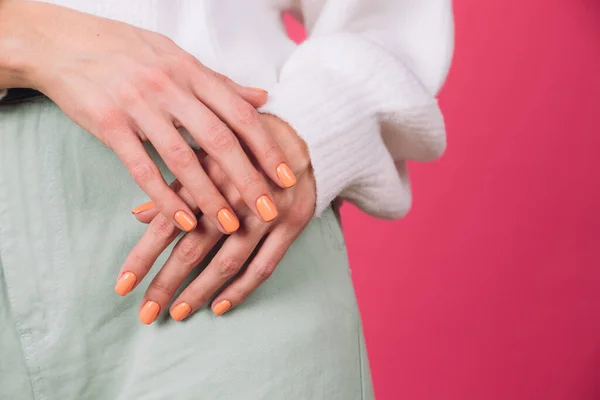 close frame of woman\'s hands with orange manicure on white sweater and pink background isolated copy space