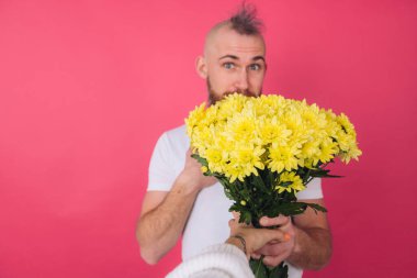 Pembe arka plandaki Avrupalı adam bir buket sarı çiçek, bahar havası, izole edilmiş, heyecanlı yüz alır.