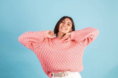 Ilık pembe kazaklı genç esmer, mavi arka planda soyutlanmış mutlu dans hareketleri.