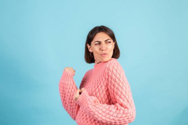 Mavi arka planda izole edilmiş koyu pembe kazaklı genç esmer Kazanan yumruğunu sıkarak kutluyor