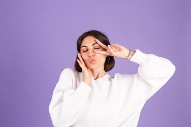 Mor arka planda izole edilmiş beyaz kazaklı genç esmer hava öpücüğü yolluyor.