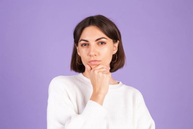 Mor arka planda izole edilmiş beyaz kazaklı genç bir esmer bir soru hakkında endişeleniyor, endişeli ve gergin.