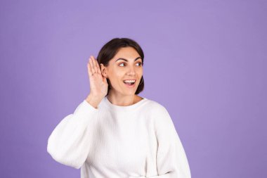 Mor arka planda izole edilmiş beyaz kazaklı genç esmer. Kulak fotokopi aletiyle söylediklerini duymaya çalış.