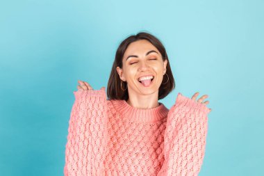 Pembe kazaklı genç esmer, mavi arka planda soyutlanmış neşeli, şakacı, kapalı gözlü dilli.