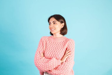 Mavi arka planda izole edilmiş pembe kazaklı genç esmer. Çapraz elli. Gülümse.