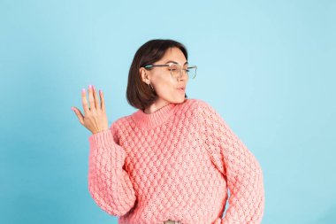 Pembe süveterli genç esmer, mavi arka planda izole edilmiş, gülümseyen gözlükler takıyor.