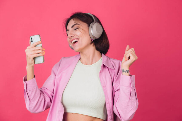 Happy positive woman in headphones on pink red background positive dancing moving enjoying sound