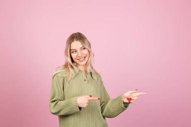 Pembe arka planda sıradan örülü süveter giyen güzel Avrupalı bir kadın işaret parmağıyla çok mutlu ve heyecanlı bir nokta.  