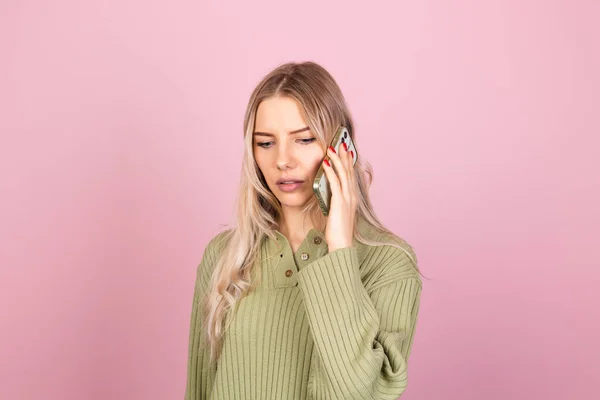 穿着粉色背景休闲装毛衣的漂亮的欧洲女人孤零零地拿着电话 带着好奇困惑严肃的面孔交谈 — 图库照片