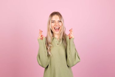 Pembe arka planda gündelik süveter giyen güzel Avrupalı kadın özel anı bekle, şans dile, dilek hareketi yap. 