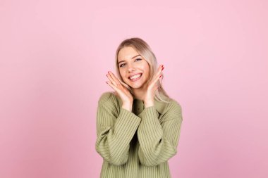 Pembe arka planda gündelik süveter giyen güzel Avrupalı kadın. Kameraya mutlu bir bakış.