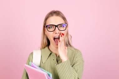 Pembe arka planda sıradan süveter giyen güzel Avrupalı bir kadın. Not defterleri bağırıyor. Ağızdan bağırışlar, eğitim konsepti.