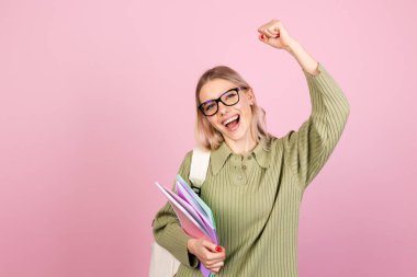 Pembe arka planda sıradan süveter giyen güzel Avrupalı bir kadın yumruğunu sıkmış, jest eğitimi kavramını sergiliyor.