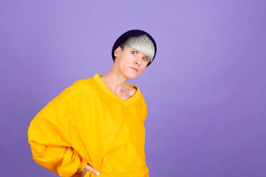 Mor arka planda, sarı büyük ceket ve şapka giymiş şık Avrupalı kadın.