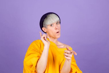 Mor arka plandaki zarif Avrupalı kadın seni mutlu yüzlü kameraya işaret ediyor.