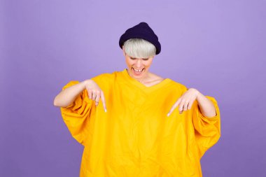 Mor arka planda şık Avrupalı bir kadın parmaklarını göstererek reklamını yapıyor, şaşırmış yüzünü ve ağzını açıyor.