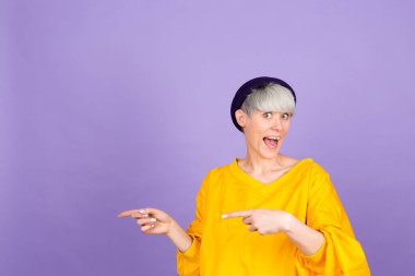 Mor arka planda şık Avrupalı bir kadın sol elini göstererek reklamını yapıyor, şaşırmış yüzünü ve ağzını açıyor.
