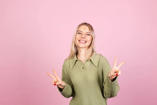 かなりヨーロッパの女性でカジュアルなセーターでピンクの背景笑顔でカメラに平和ジェスチャー勝利サインを行う — ストック写真