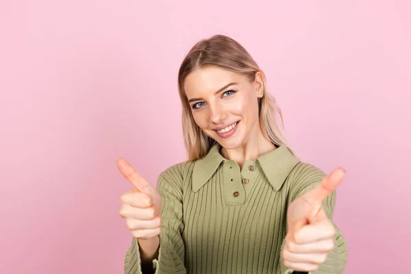 かなりヨーロッパの女性でカジュアルなセーターでピンクの背景幸せな励起ショー親指アップとともに大笑顔 — ストック写真