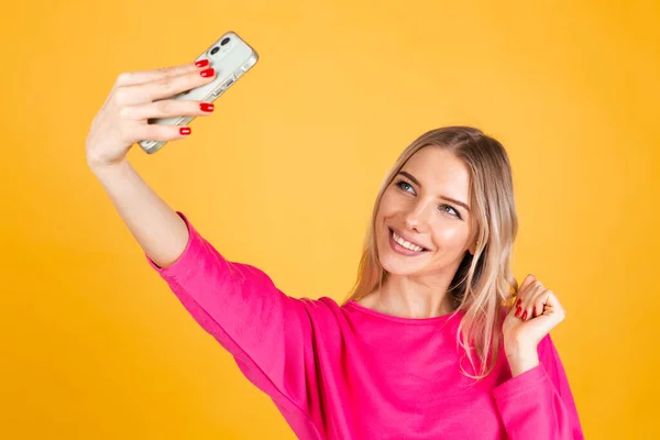 Pretty european woman in pink  blouse on yellow background holding shopping bags taking selfie on mobile phone happy emotions