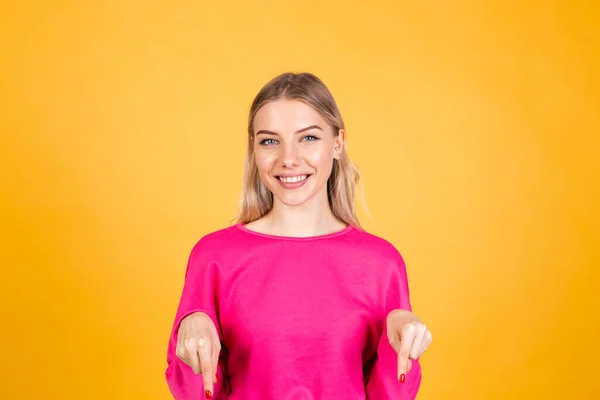かなりヨーロッパの女性でピンクブラウス上の黄色の背景幸せな励起陽気なポイントダウンとともにインデックス指 — ストック写真